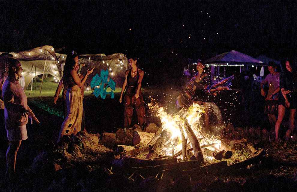 several fire performers stand together at night around a large campfire.