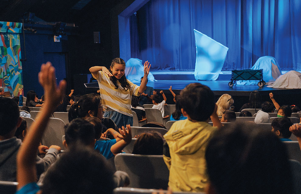 a person in a yellow shirt and blue pants standing in a room with a stage and a stage with a blue curtain