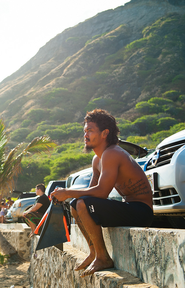 a person sitting at the edge of a stone wall looking over the view of the beach with the mountains in the background