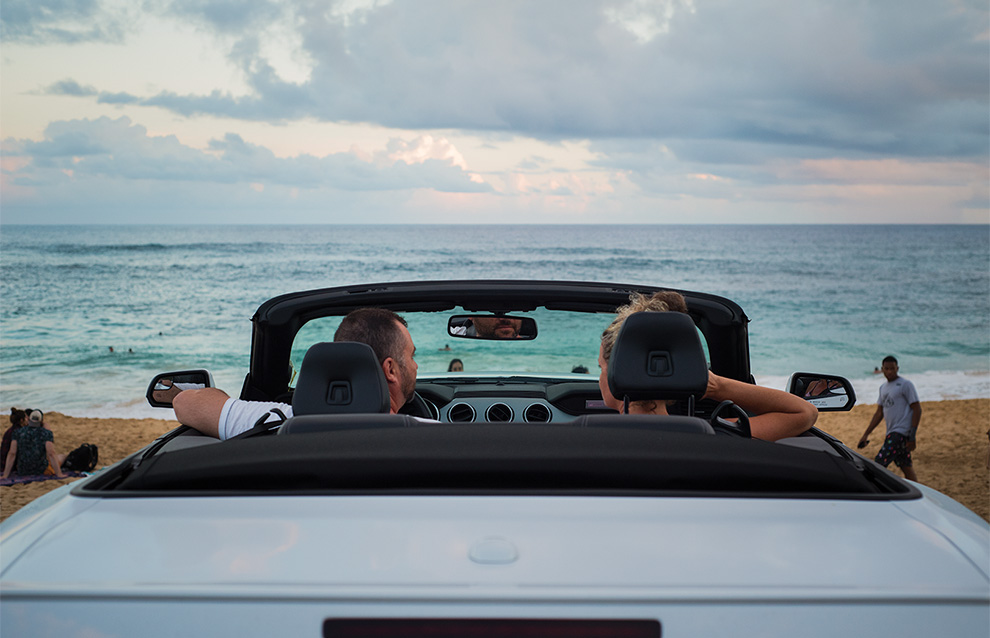 two people sitting in a convertible car watching the ocean