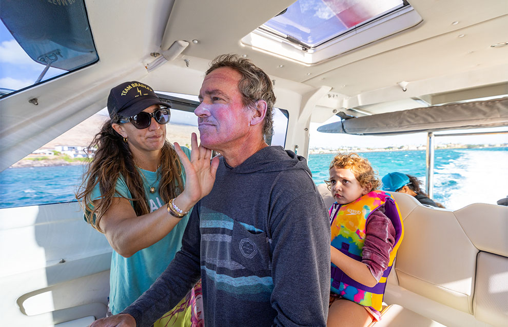 a person applying sunscreen to another person, inside a boat
