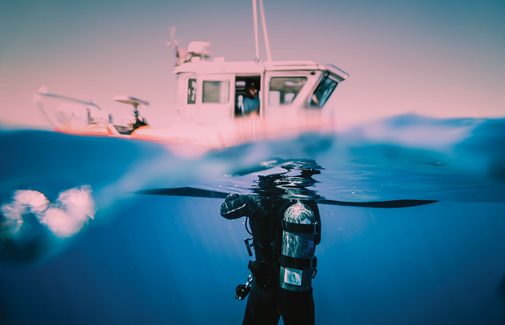 a person in a scuba suit under water with a boat in the background