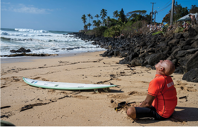 a person sitting on a beach looking up at a surfboard