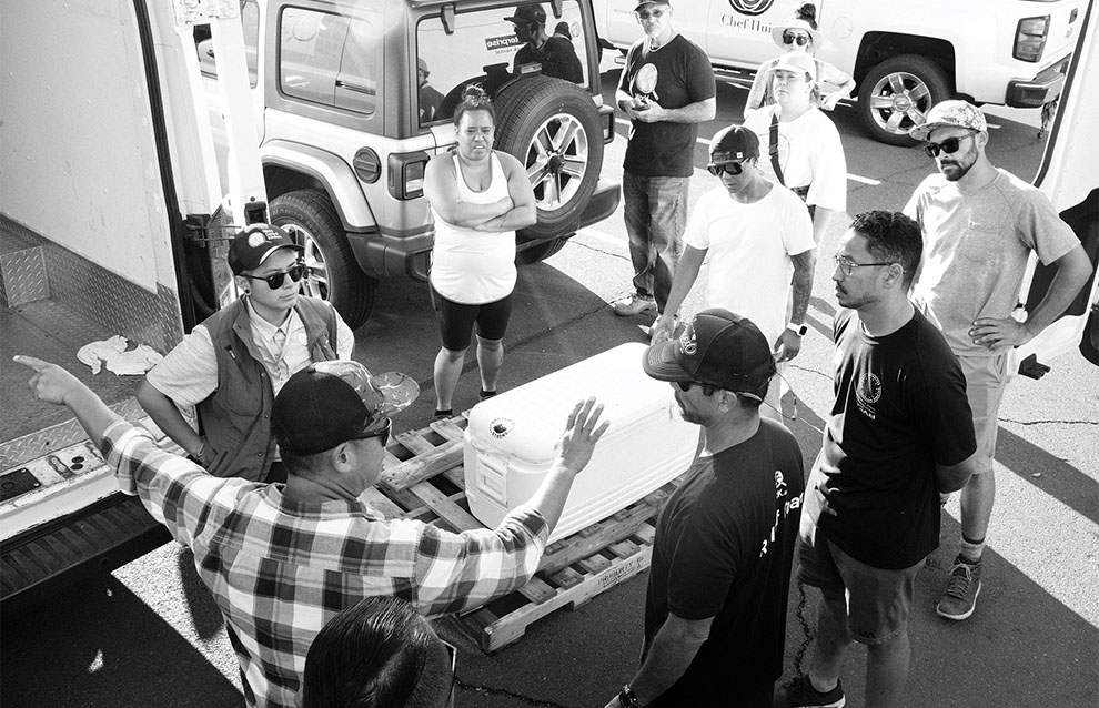 a group of people standing around a pallet with a white cooler