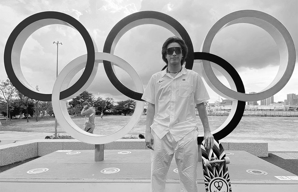 a person holding a skateboard in front of the olympic rings