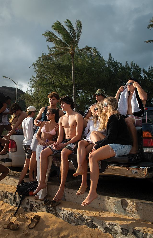 a group of people sitting at the back of a truck looking over to the sunset at the beach