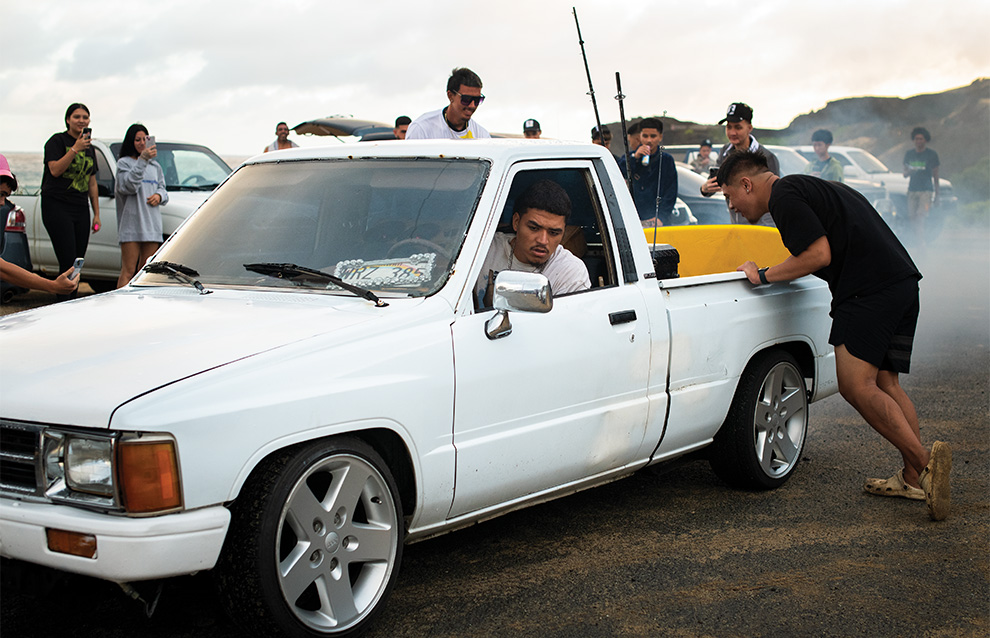 a group of people watching a person drive a white truck with smoking tires
