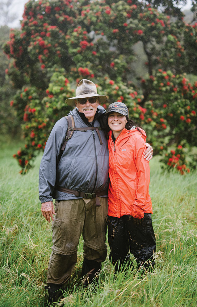 two people stand on grassy lands in front of a tree