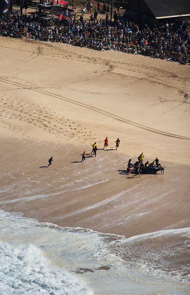 an aerial photo of a beach shore with people gathered to watch surfers