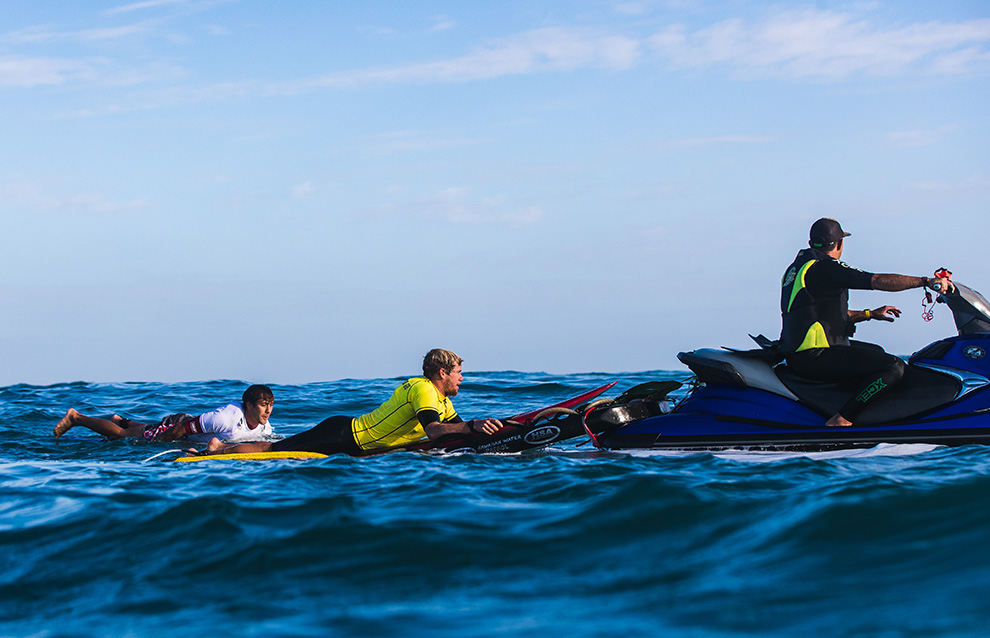 a person on a jet ski aiding two surfers to get to the shore